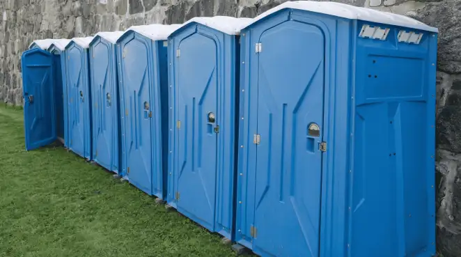 Row of blue portable toilets lined up on grass against a stone wall for event sanitation in Baltimore, MD