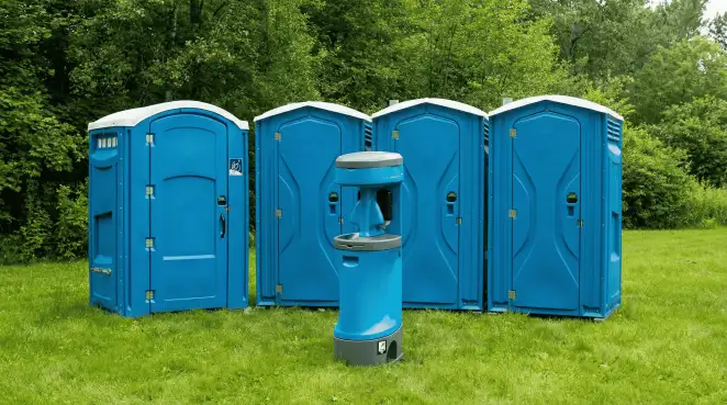 Four blue portable toilets and a matching hand washing station on grass near trees, a common sight at local outdoor events in Baltimore, MD