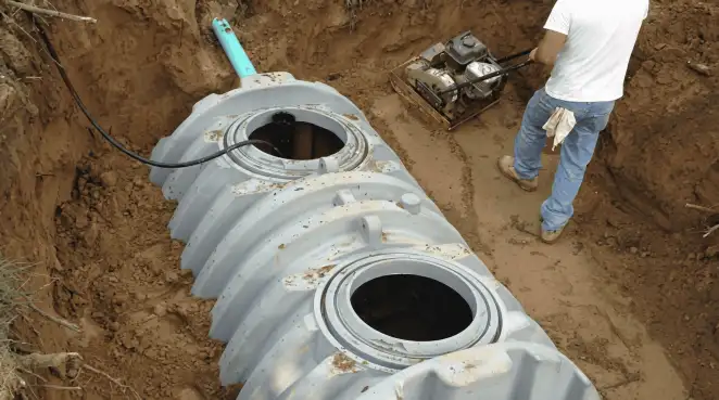Septic tank installation showing a technician compacting soil around a new poly septic tank in an excavation pit in Baltimore, MD